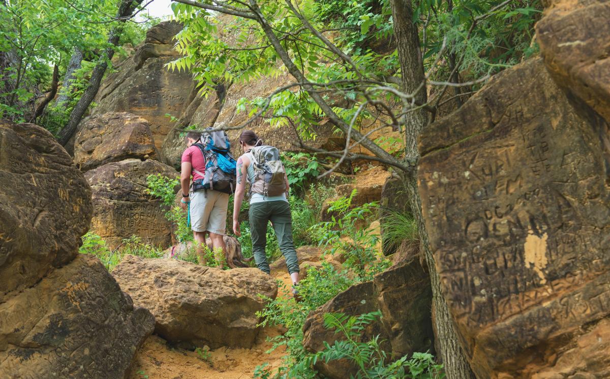 couple hiking through trees and red sandstone rock