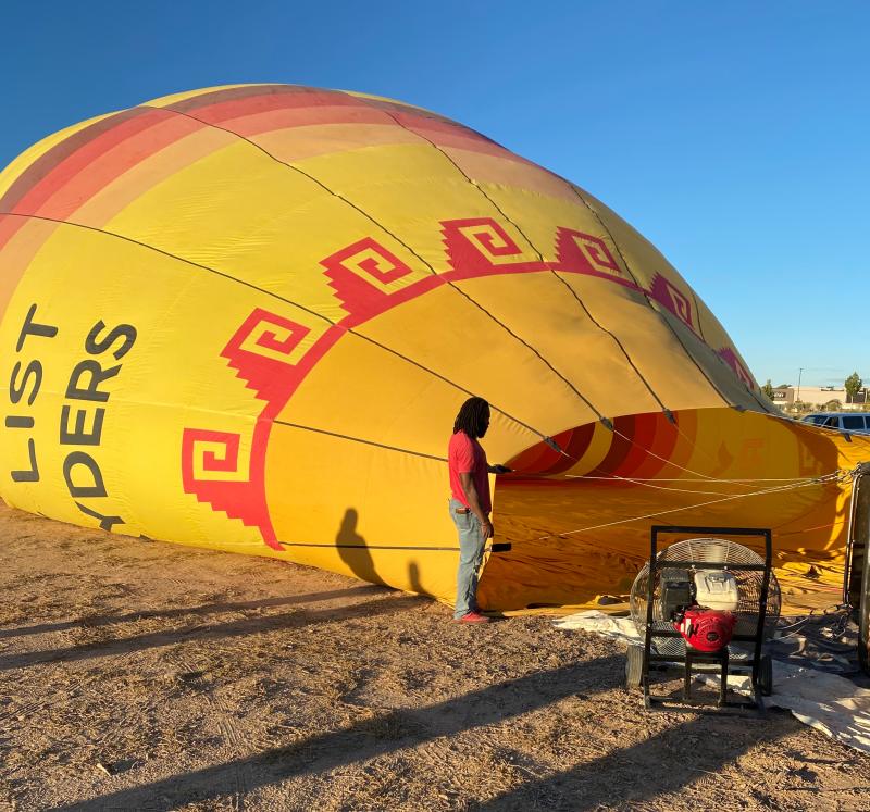 A hot air balloon envelope is being filled with air by a large industrial fan