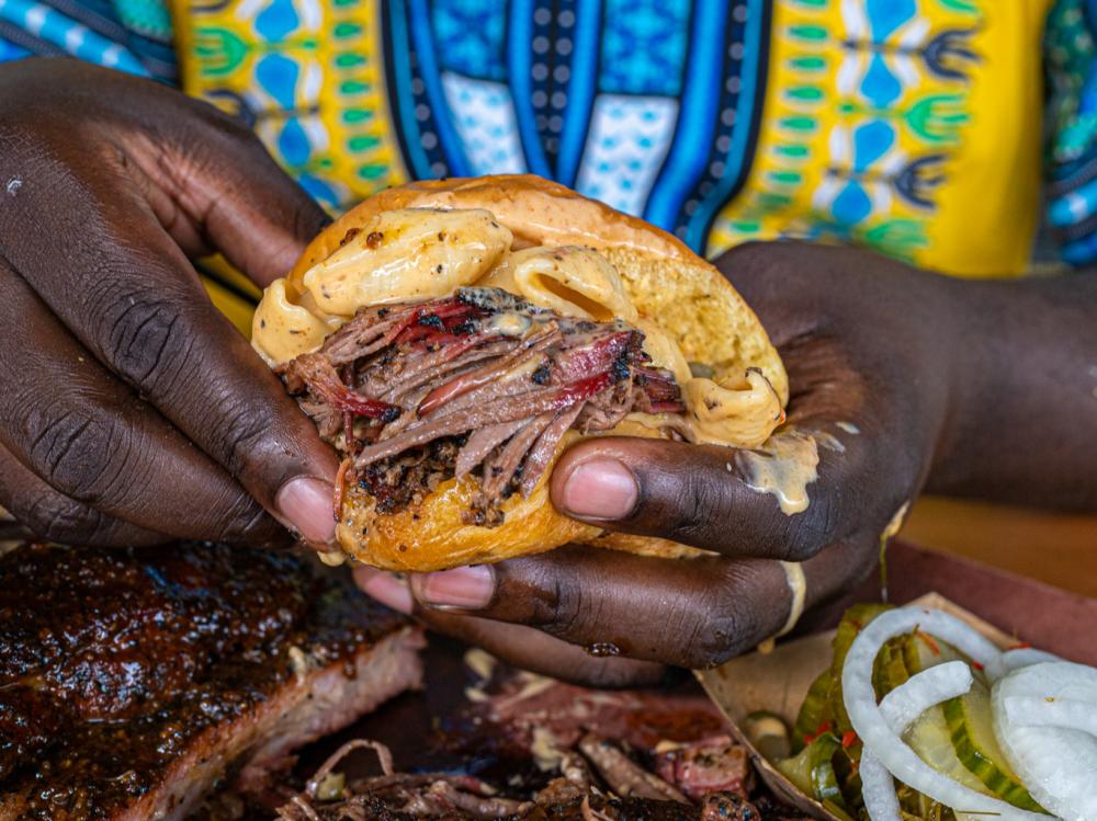 Photo of man's hands holding a brisket sandwich towards the camera at La Barbecue