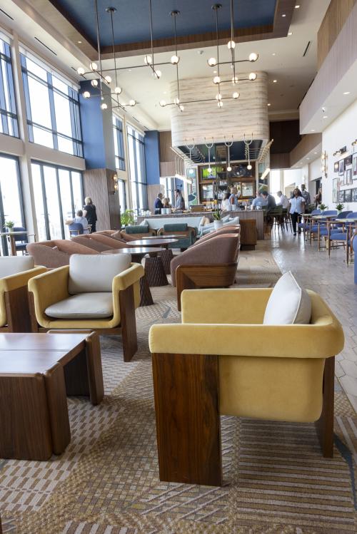 Modern seating area inside Vesper Sky Lounge at Trilogy Hotel in downtown Huntsville, featuring colorful lounge chairs, large windows, and a bar.