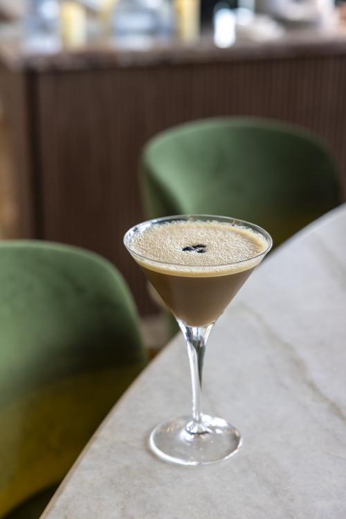 Espresso martini garnished with coffee beans on a marble tabletop at Vesper Sky Lounge, with green seating in the background.