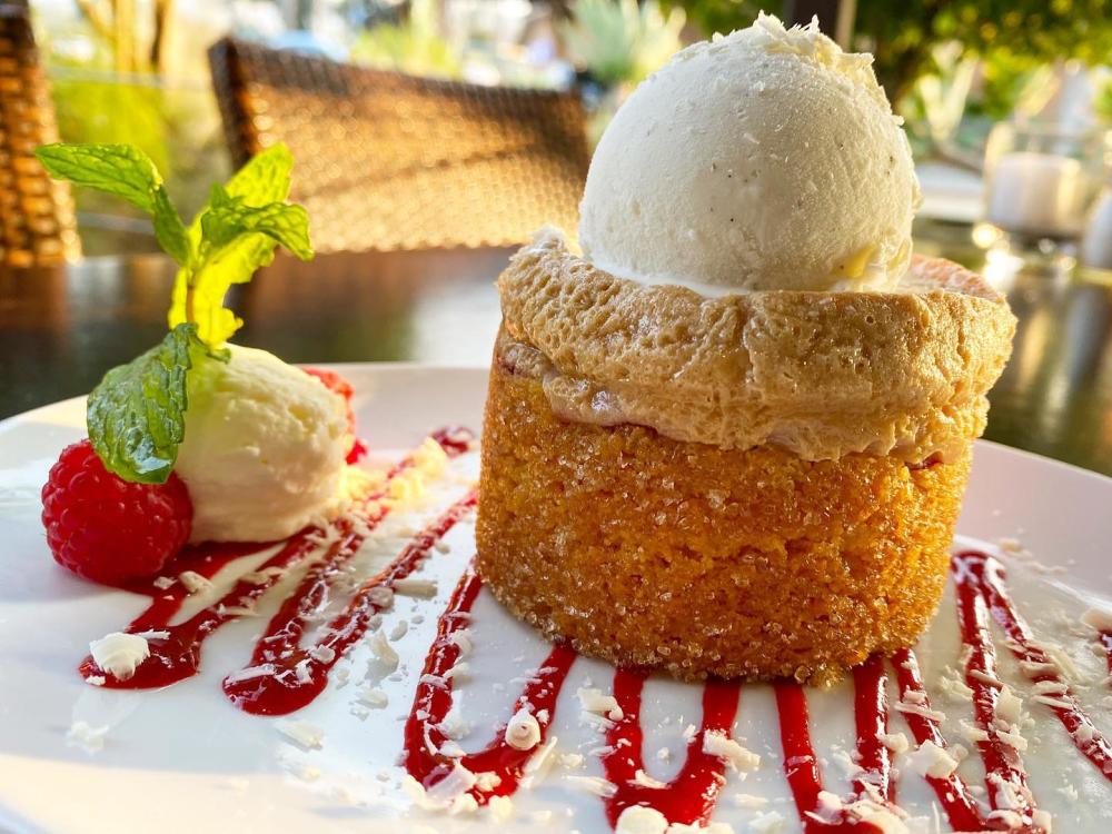 Image of butter cake served atop a drizzle of strawberry syrup and next to two berries and a dollop of whipped cream.