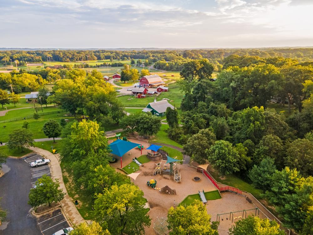 a view of a playground and park with fields and a red barn in the background/