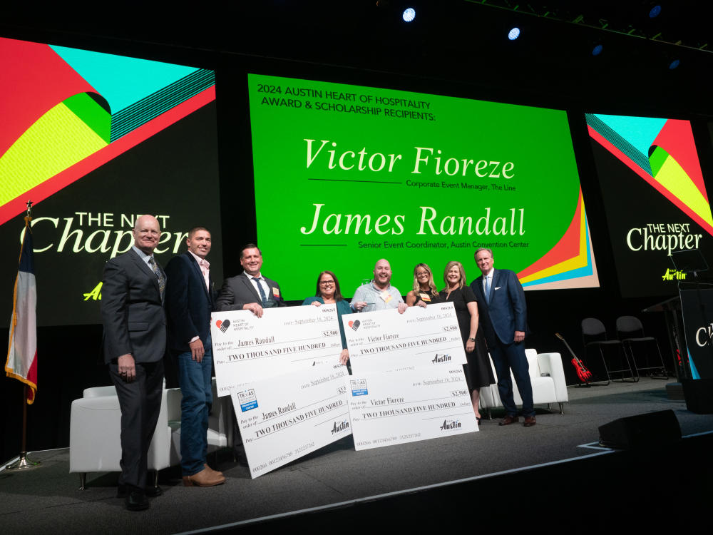 Professional men and women standing on a large stage with giant checks signifying a scholarship award.