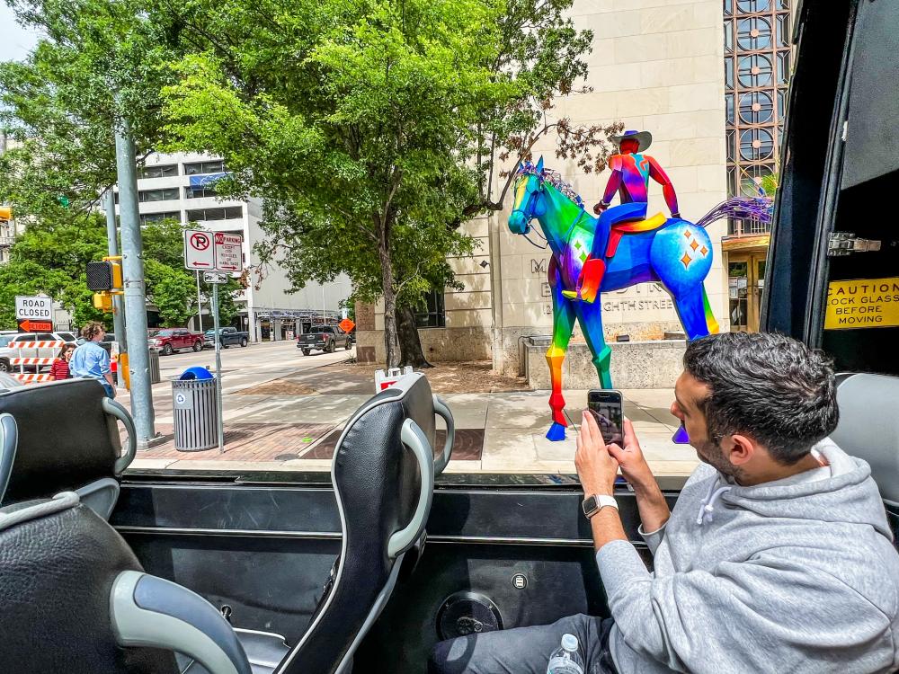 Man taking a picture of a statue with his phone while sitting in an open air vehicle.