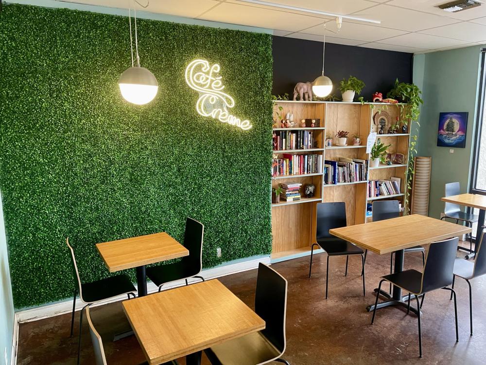 Minimally decorated cafe with greenery wall and neon sign with words "Cafe Creme".