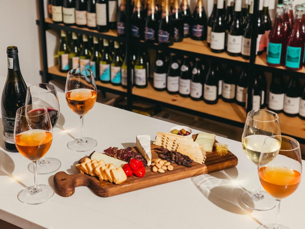 Shiny wine glasses filled with different colors of wine next to a full grazing board of cheeses, crackers and snacks.