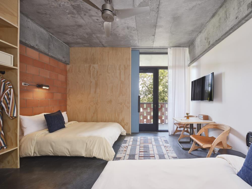 Standard bedroom at the Carpenter Hotel with a minimalist design featuring two queen beds and a wooden bench.