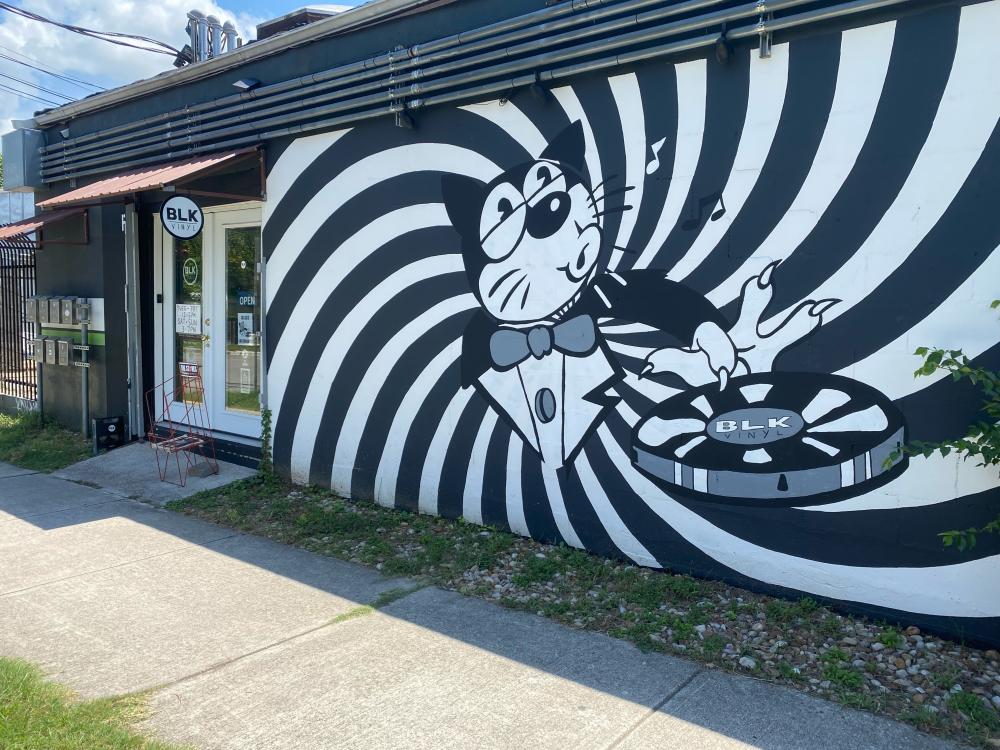 Photo of the exterior of BLK Vinyl  with a black and white mural of a cat in a tuxedo in the center of a spiral design, spinning a record with one finger