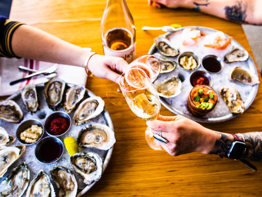 Two people clink wine glasses over trays of oysters at Parkside in Austin Texas