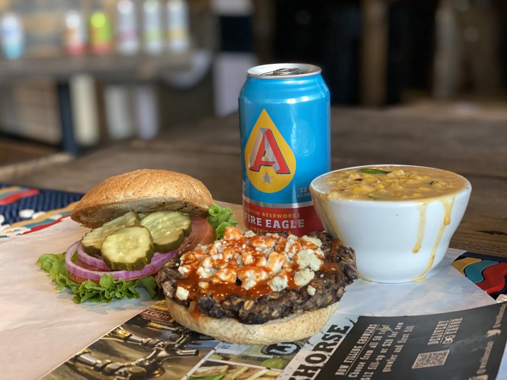 Open-faced signature buffalo burger next to Austin Eastciders can and messy cup of soup.
