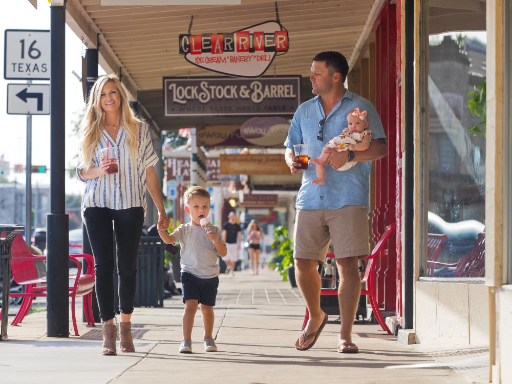 Family walking past Main Street shops in downtown Fredericksburg with ice creams in their hand.