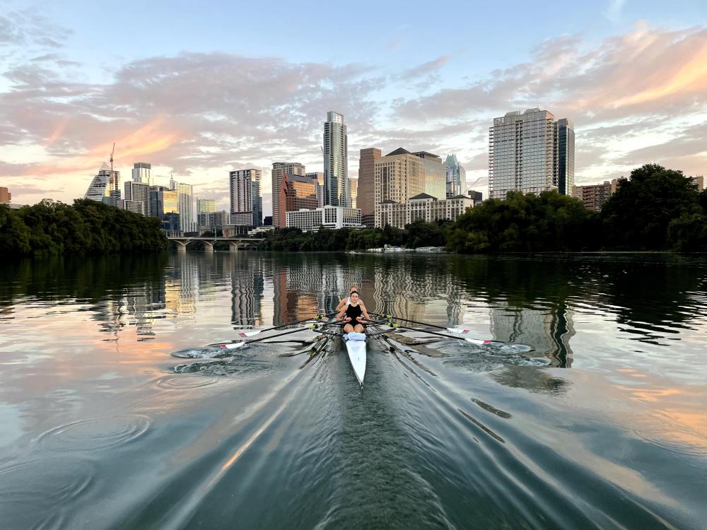 Rowers moving towards the downtown skyline on glassy, reflective water.