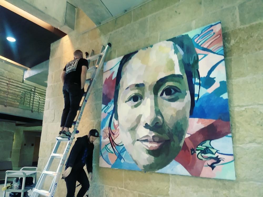 two men work on large painting of a woman's face for the People's Gallery in Austin Texas