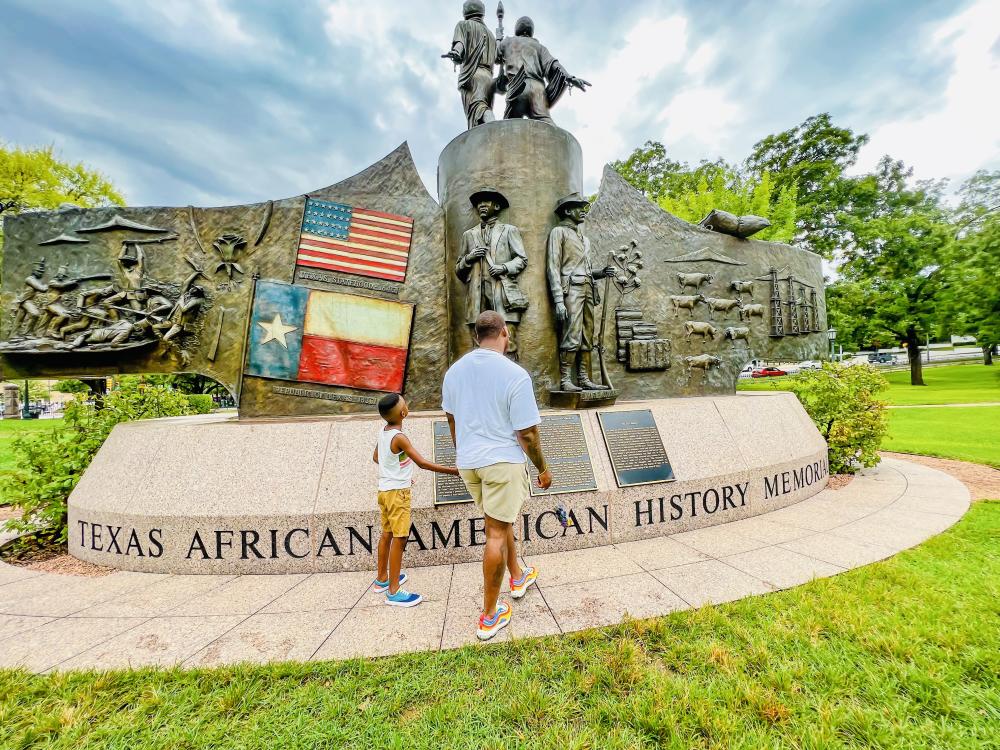 Father and son walking in front of the Texas African American History Memorial at the Texas State Capitol.
