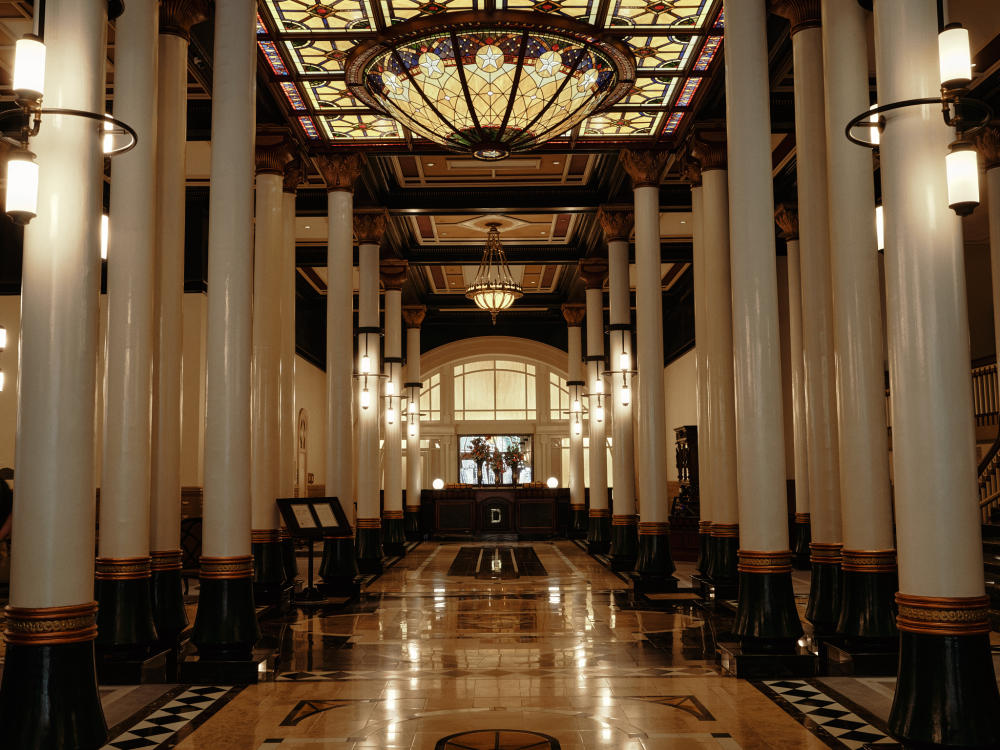 Main foyer of the Driskill Hotel with towering columns and ornate flooring and glasswork in the ceiling.