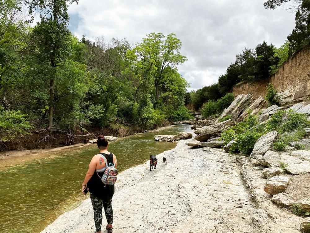 Woman with tattoos and a backpack looking back at her dogs walking along the creek bed at Walnut Creek Metro Park.