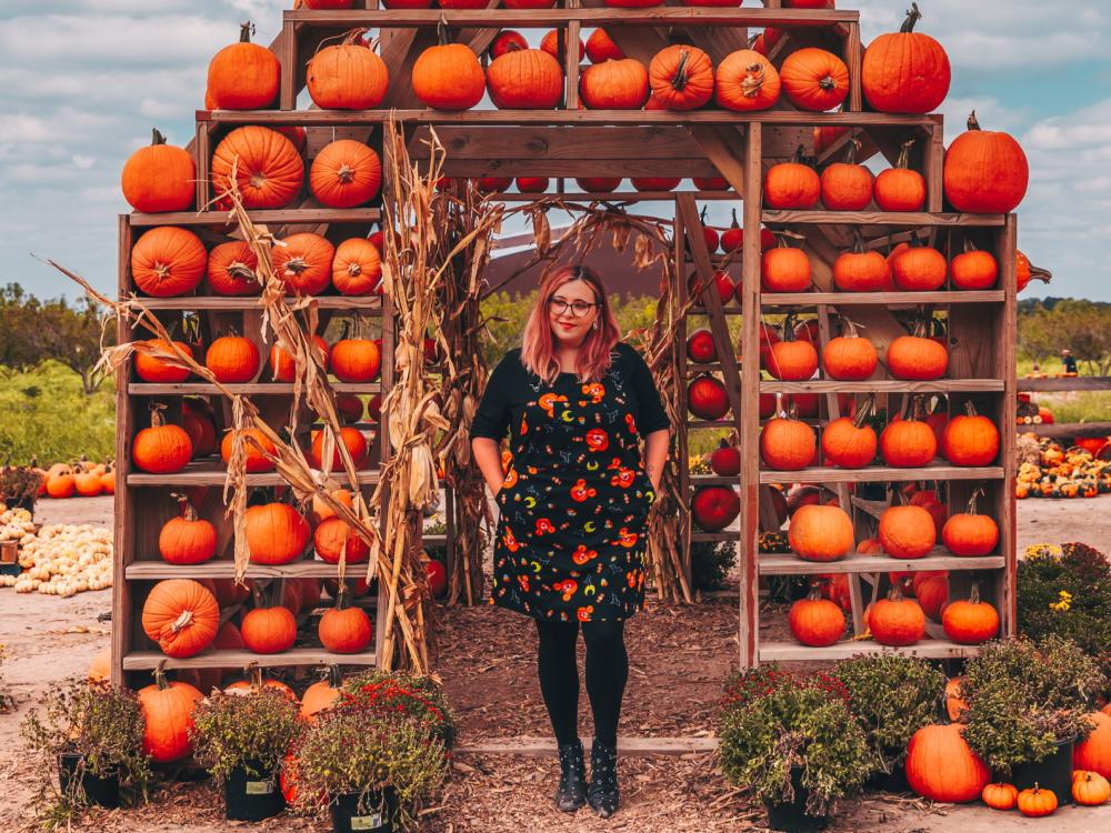 Woman stands in front of a large Fall pumpkin display at Sweet Eats Fruit Farm near Austin Texas