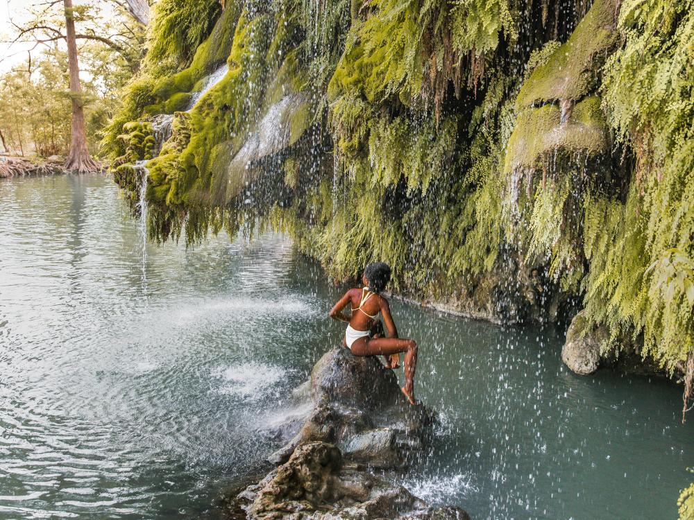 Woman sitting on a rock under waterfall at Krause Springs near Austin Texas