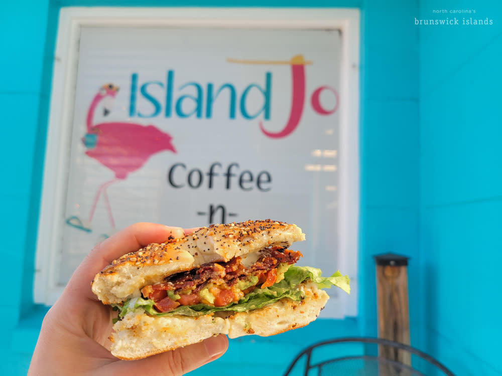 An BLT avocado sandwich on an everything bagel in front of a blue building