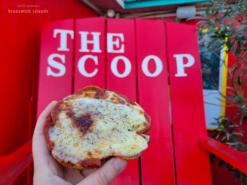An open-face bagel covered in pepperoni and cheese in front of a large red chair