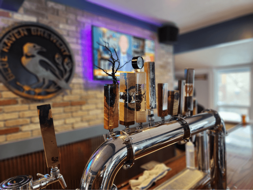 Artisanal beer tap handles in focus with the Blue Raven Brewery logo blurred in the background, inside the brewery's inviting premises.