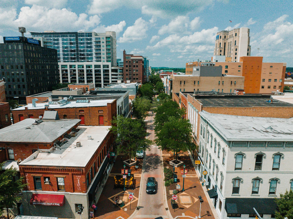 An aerial view of the Kalamazoo Mall showcases a blue sky with white clouds atop older, brick buildings, that are on a brick street.