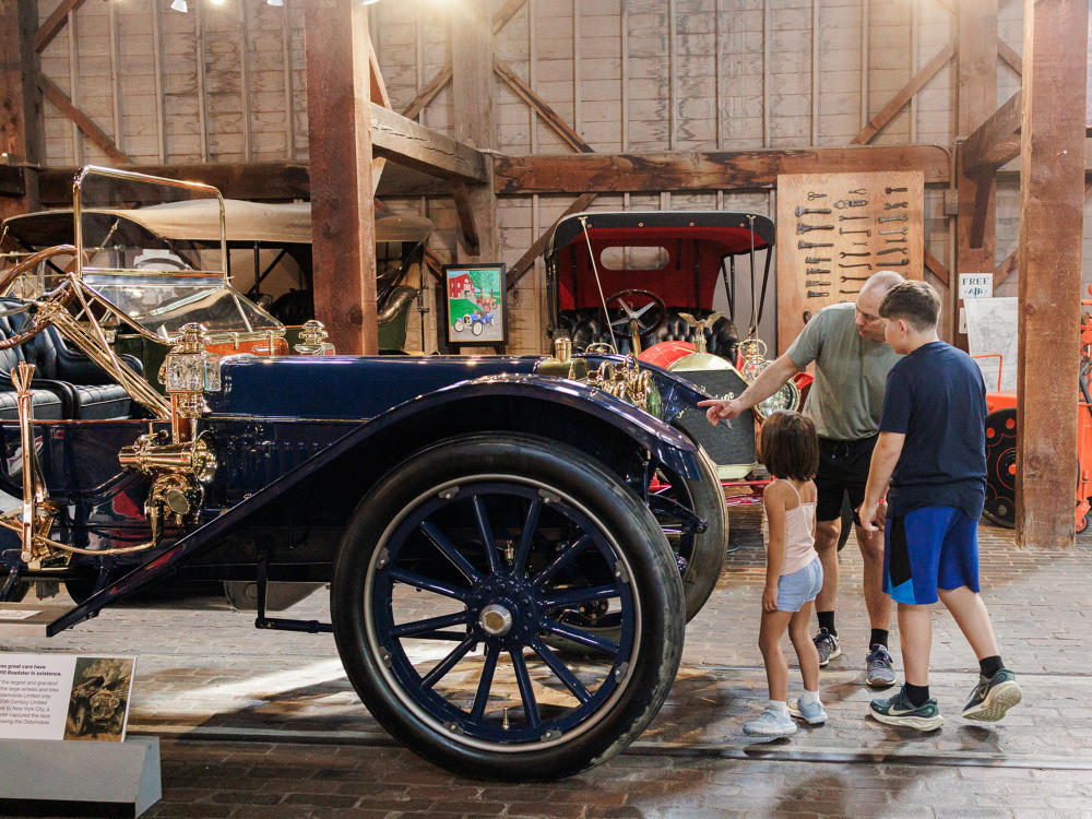 A man points inside the engine of a car for his two children to view at the Gilmore Car Museum.