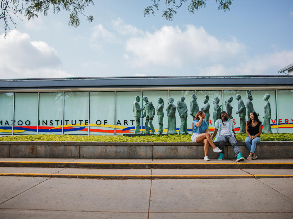 Three individuals sit at the base of a sculpture outside the Kalamazoo Institute of Arts.