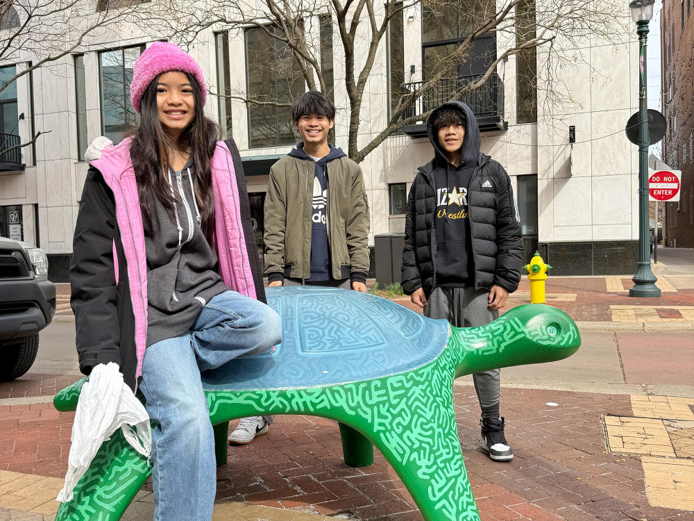 Three kids sit on a turtle statue that is located on the Kalamazoo Mall in Downtown Kalamazoo.