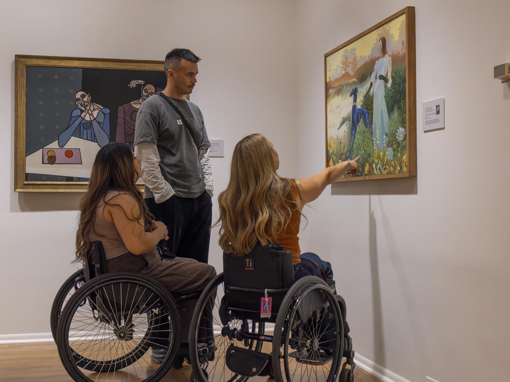 Two women in wheelchairs and a man admire a painting in the permanent gallery of the Kalamazoo Institute of Arts.