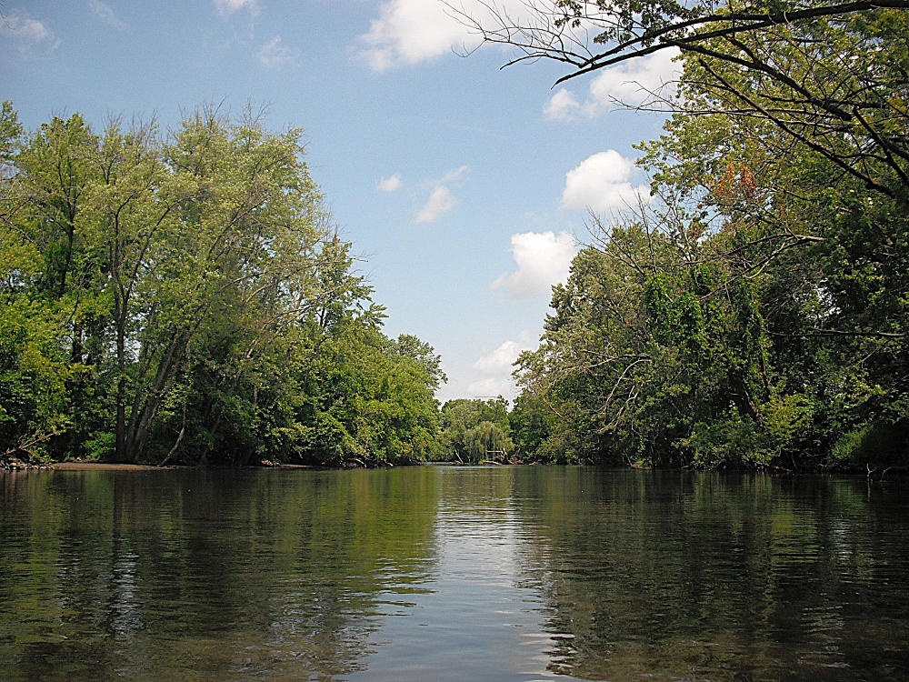The Kalamazoo River between Comstock and Parchment offers serene views of blue skies and green trees on the banks.