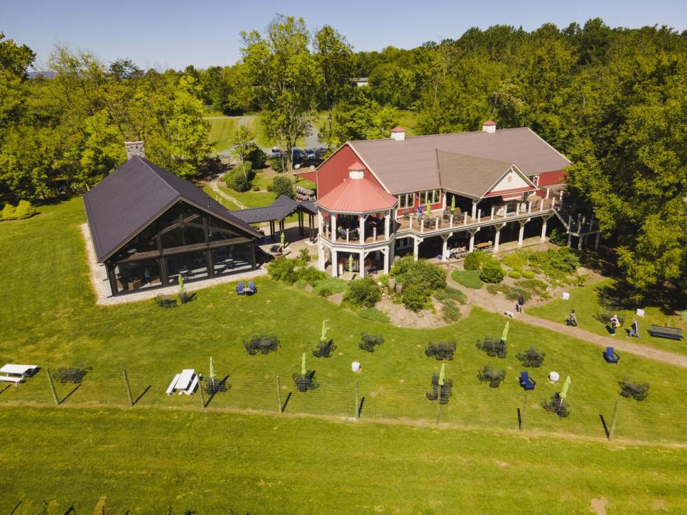 Aerial view of Cana Vineyards & Winery in Middleburg, Virginia, the venue for the Budbreak Festival, with a red-roofed tasting room, open-air pavilion and manicured grounds surrounded by spring trees
