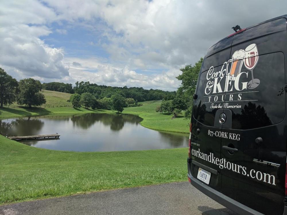 Cork & Keg Tours Mercedes Sprinter van parked at a Loudoun County winery overlooking a scenic pond and rolling vineyard hills