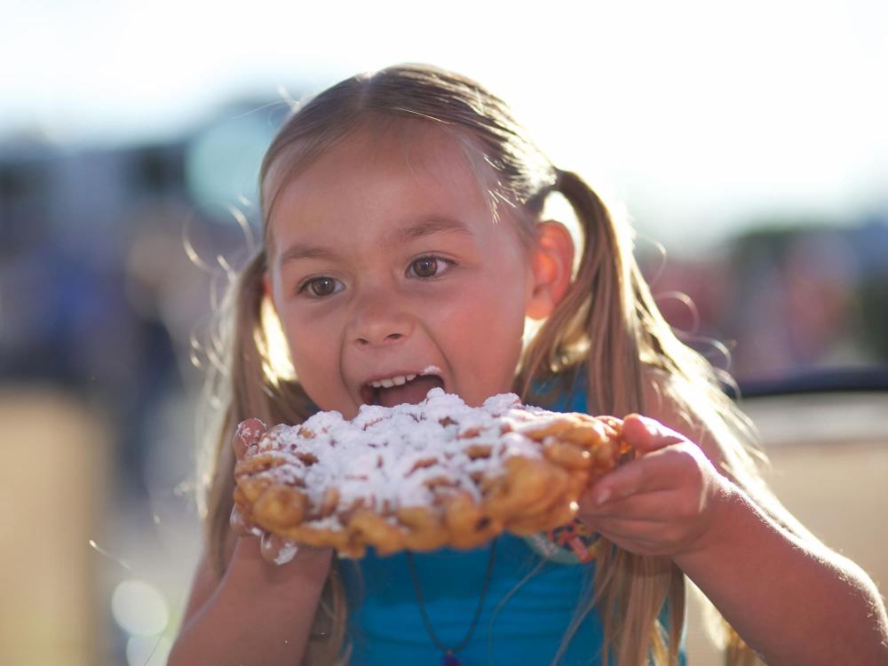 Little girl with pigtails eating funnel cake at Wichita Riverfest in downtown Wichita