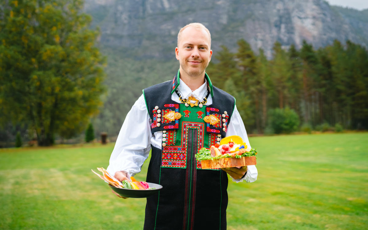 Mann i Setesdalsbunad holder opp matfat fra Sølvgarden. Fjell i bakgrunnen