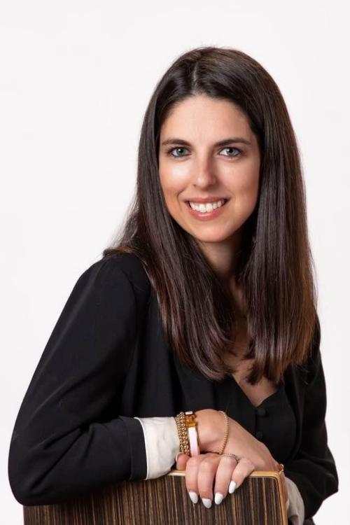 Professional Headshot of woman with dark brown hair, smiling, wearing a black longsleeve blouse.