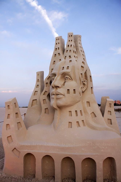Portrait of a sand sculpture that depicts a head and neck of a person that is divided into what looks like city buildings.