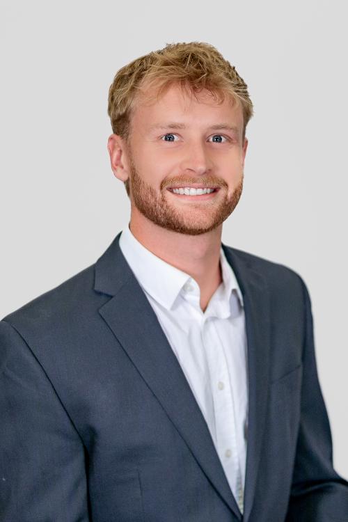 Smiling man with a beard wearinig a suit jacket and white button shirt