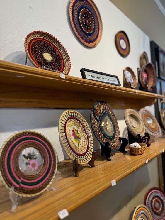 Colorful, woven plates are on display at Hands Gallery. Next to them is a plaque that reads "Fiber Arts by Pat Moretz."