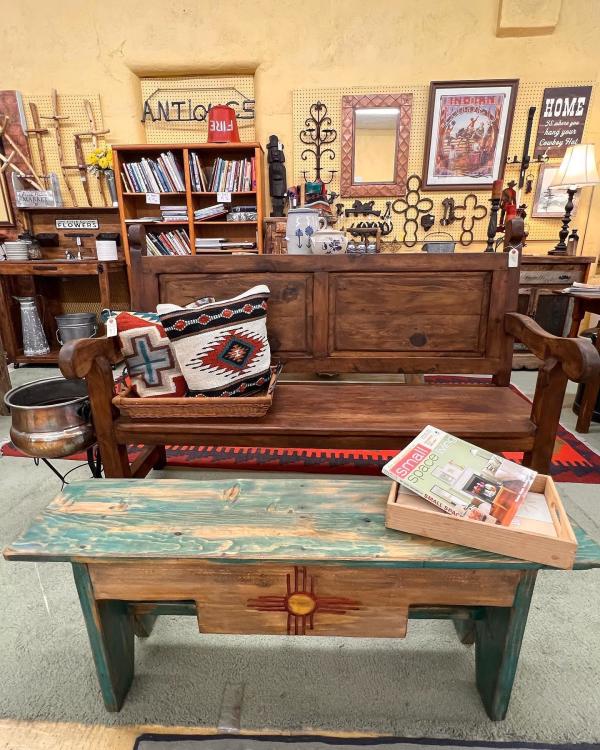 A look inside A Few Old Things Antiques and Collectibes. A wooden bench with a zia symbol sits in front of a wooden bench, with other furniture and books in the background.