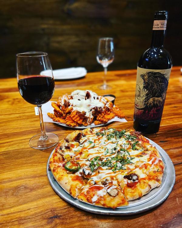 Pizza, waffle fries and red wine in a glass with a wine bottle at Jupiter Pizza and Waffles