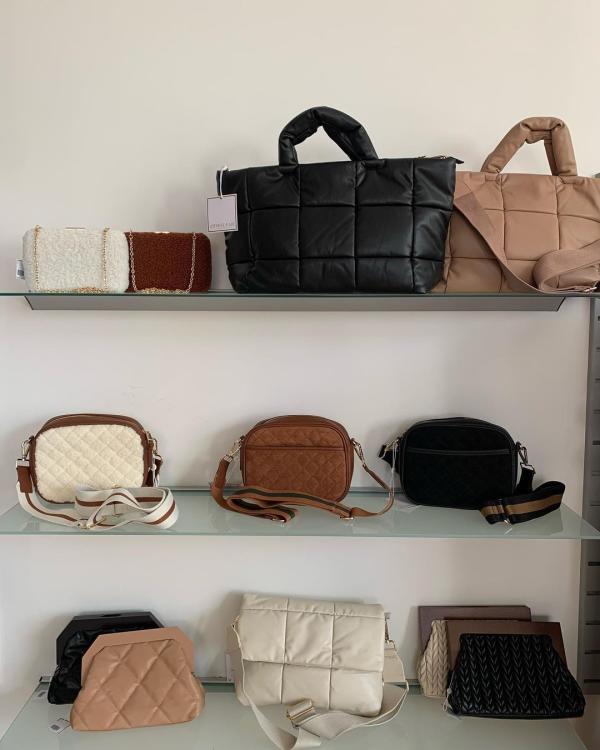 Various size purses placed on three shelving units against a wall