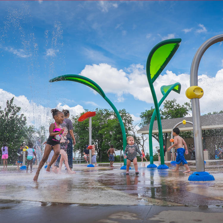 Children running around as water sprays around them on a splash pad