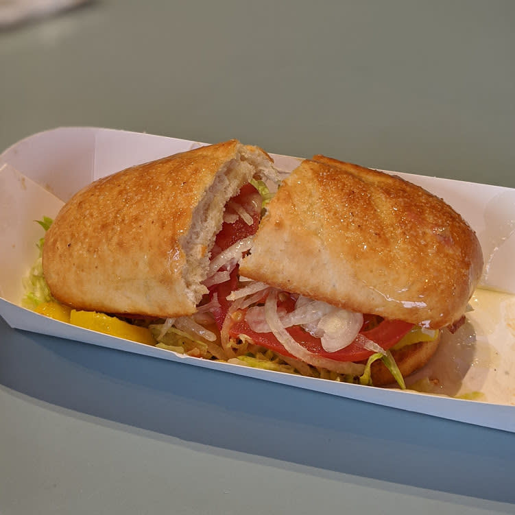 Closeup of white bread bun with tomatoes and onions and banana peppers and meat