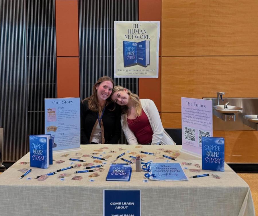 Two woman sitting at table with books and sign saying The Human Network