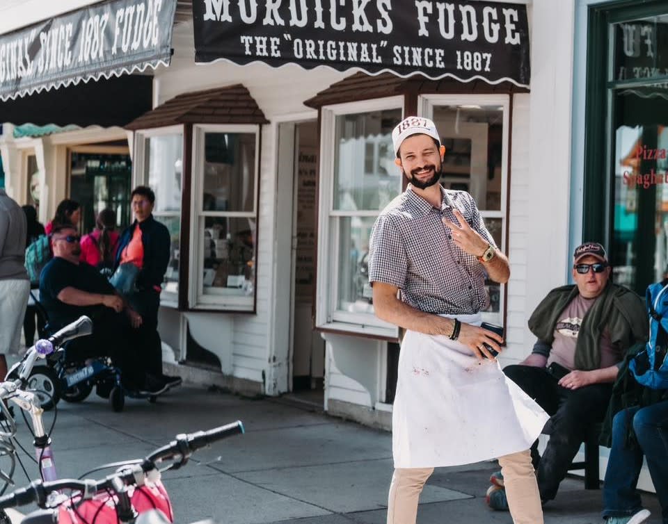 Mackinac Island fudge maker in apron standing outside by Murdick’s Fudge sign
