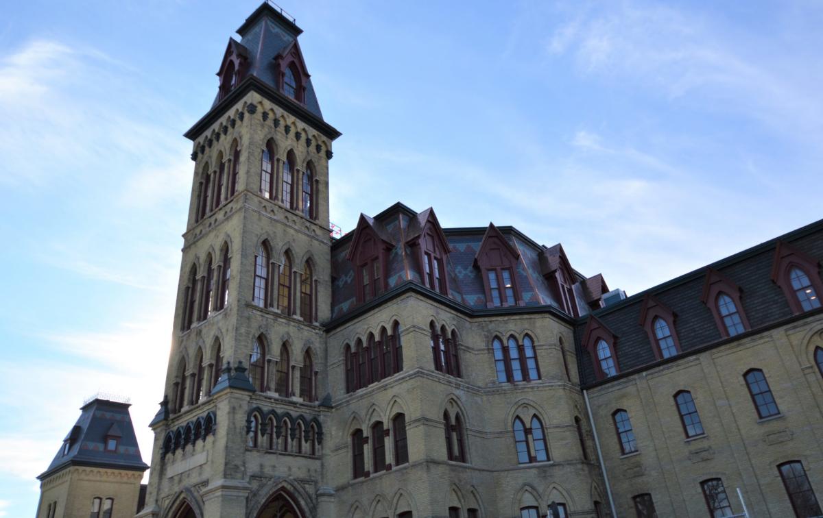 The historic Soldiers Home building in Milwaukee, featuring tall brick towers, arched windows, and a steeply pitched roof against a blue sky.