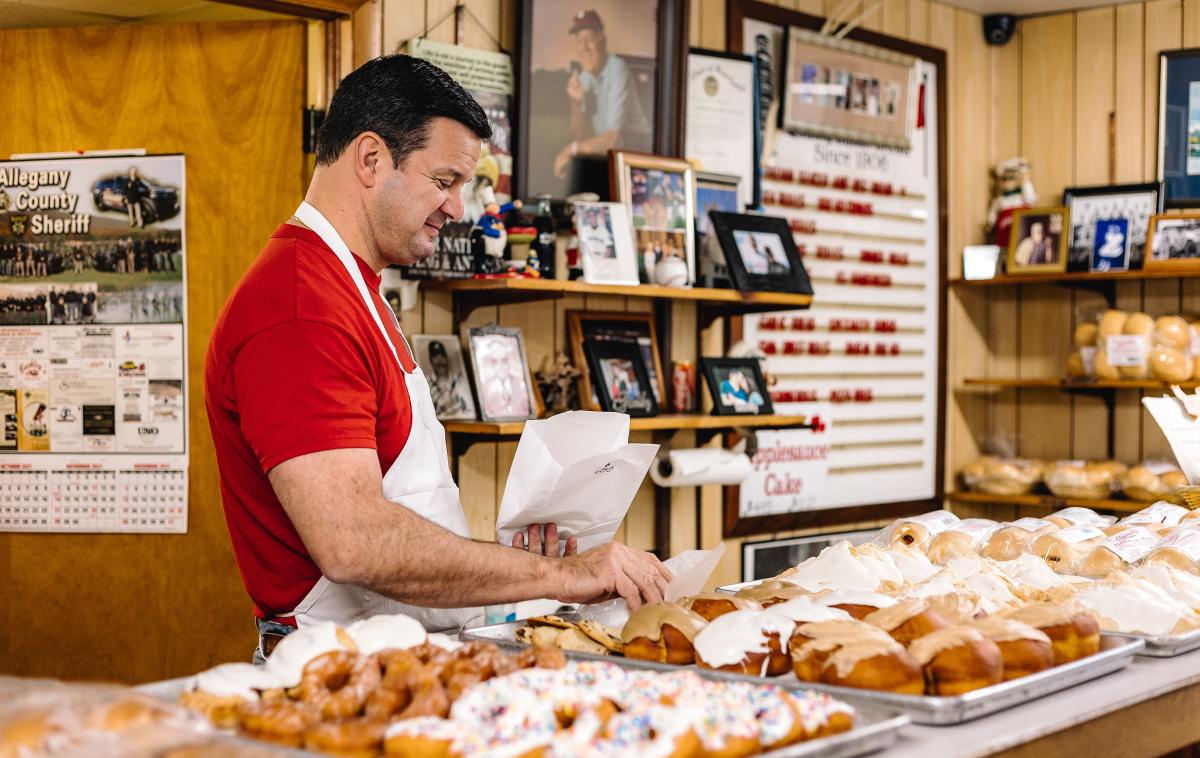A man in a red shirt grabs a donut to put in a bag for a customer.