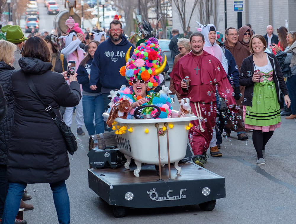 A woman sits in a bathtub during the Bockfest parade wearing a colorful pompom hat